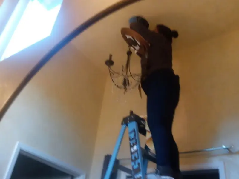 Electrician installing a chandelier in a Logan residence